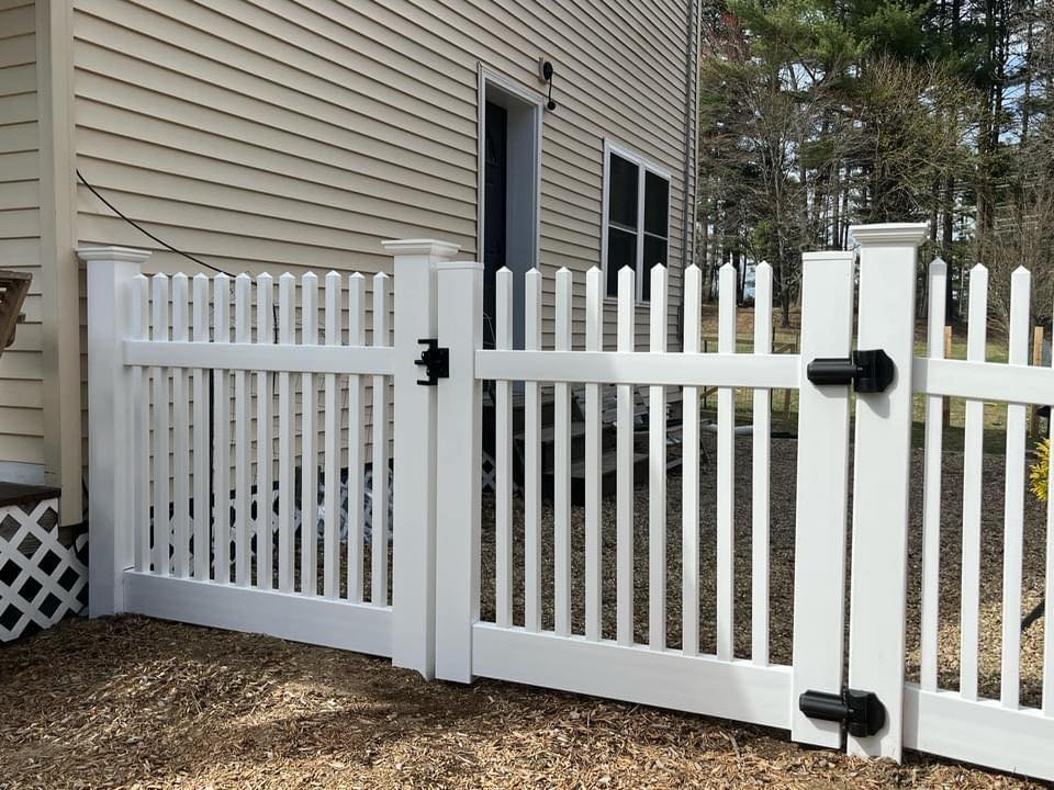 White vinyl picket fence and gate installed beside a home by New Horizon Fence